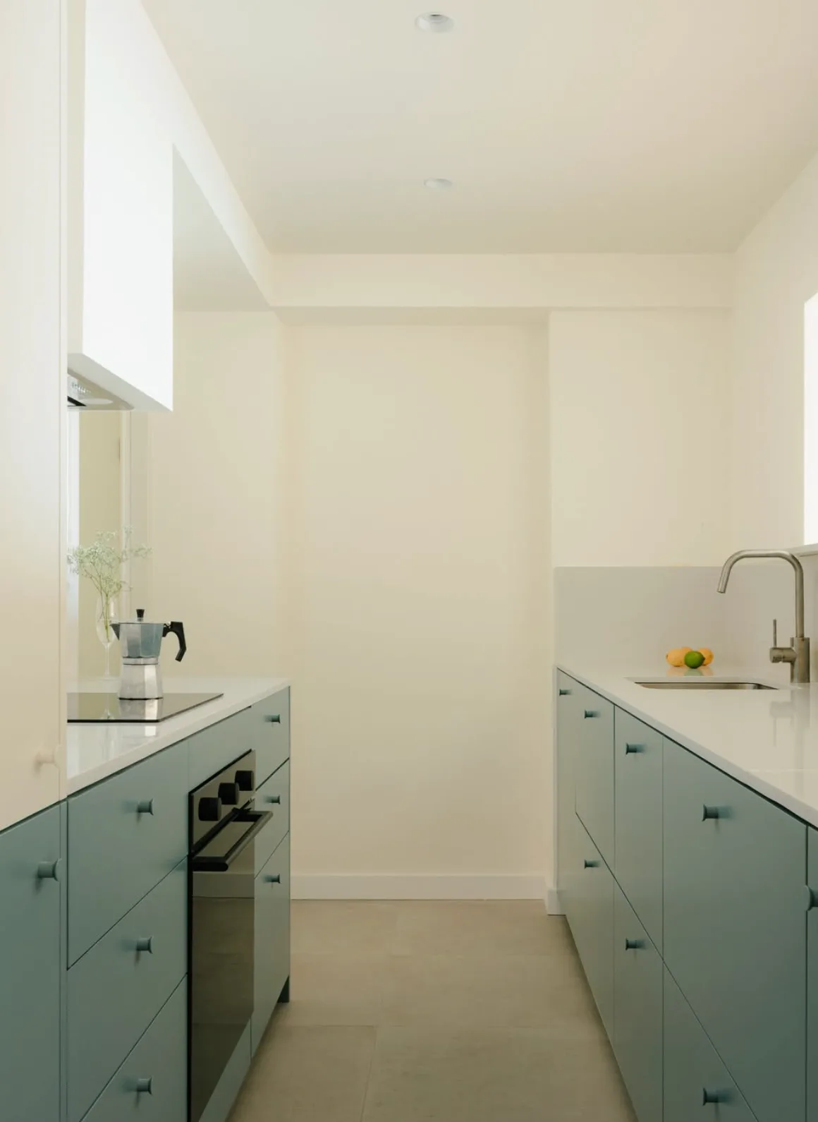 Cocina de distribución paralela con frentes azul verdoso y encimera blanca